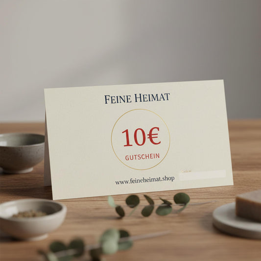 10 Euro Geschenkgutschein von Feine Heimat – Hochwertige Gutscheinkarte auf einem Holztisch mit dekorativen Schalen und Eukalyptuszweigen.