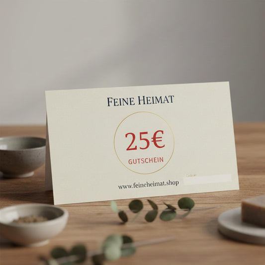 25 Euro Geschenkgutschein von Feine Heimat – Elegante Gutscheinkarte auf einem Holztisch, dekoriert mit Eukalyptuszweigen und kleinen Schalen.