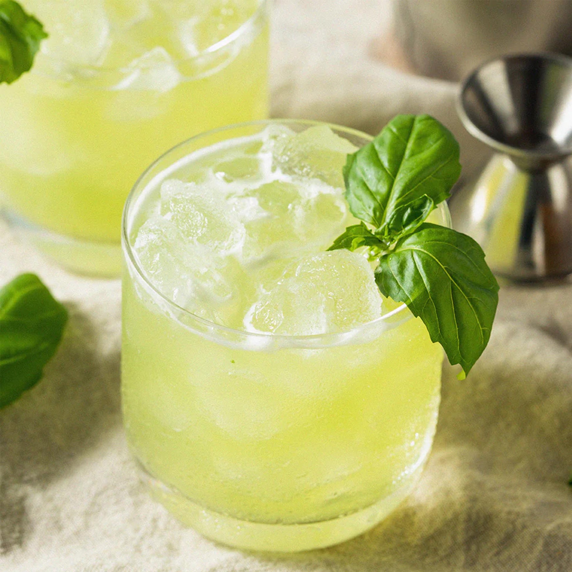 Erfrischender Sommer-Drink mit Bacanha Bio-Basilikum-Sirup, Eiswürfeln und frischen Basilikumblättern in einem Glas serviert.