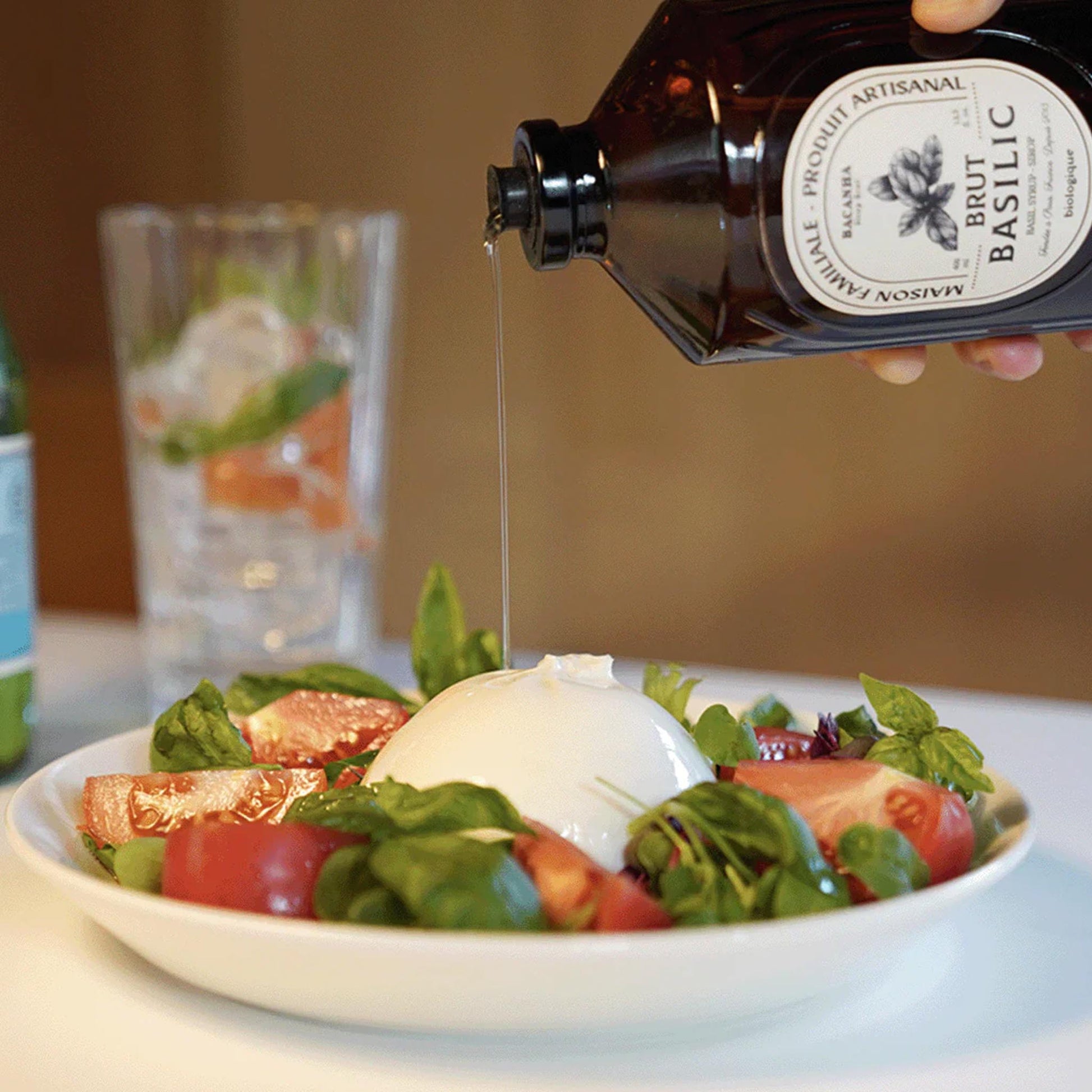 Bacanha Bio-Basilikum-Sirup wird als raffiniertes Dressing über einen frischen Tomate-Mozzarella-Salat (Burrata) mit Basilikumblättern gegossen.
