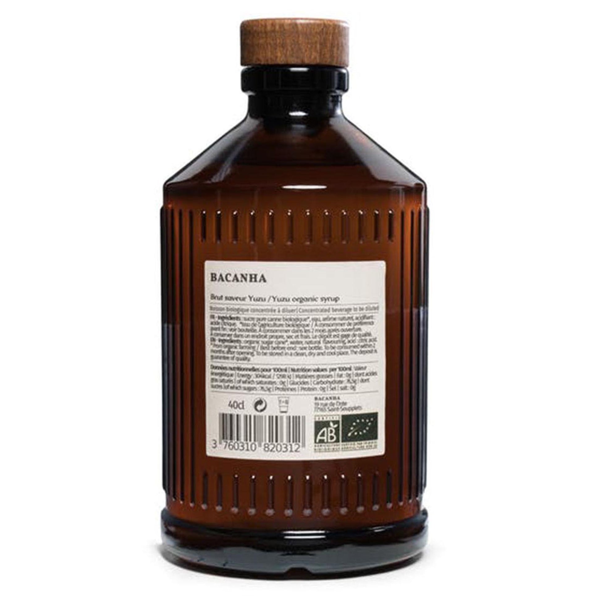 Bacanha Bio-Yuzu-Sirup (Sirop Brut de Yuzu) in der 400ml Glasflasche neben einem Glas mit Eiswürfeln, einer Zitronenscheibe und Strohhalm auf einem Holztisch.