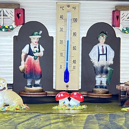 Nahaufnahme der Figuren einer Schwarzwälder Wetterstation – Detailansicht von Frau und Mann in traditioneller Tracht neben einem zentralen Thermometer mit Celsius- und Fahrenheit-Skala.