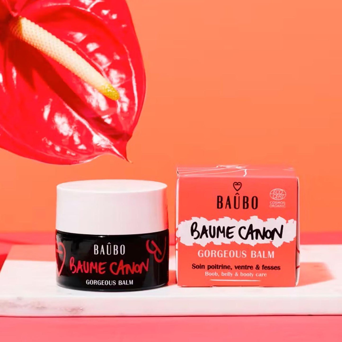 Baûbo Baume Canon Gorgeous Balm (50 ml) – Bio-zertifizierter Balsam für Brust, Bauch und Po, dekorativ präsentiert auf Marmor neben einer roten Anthurie.