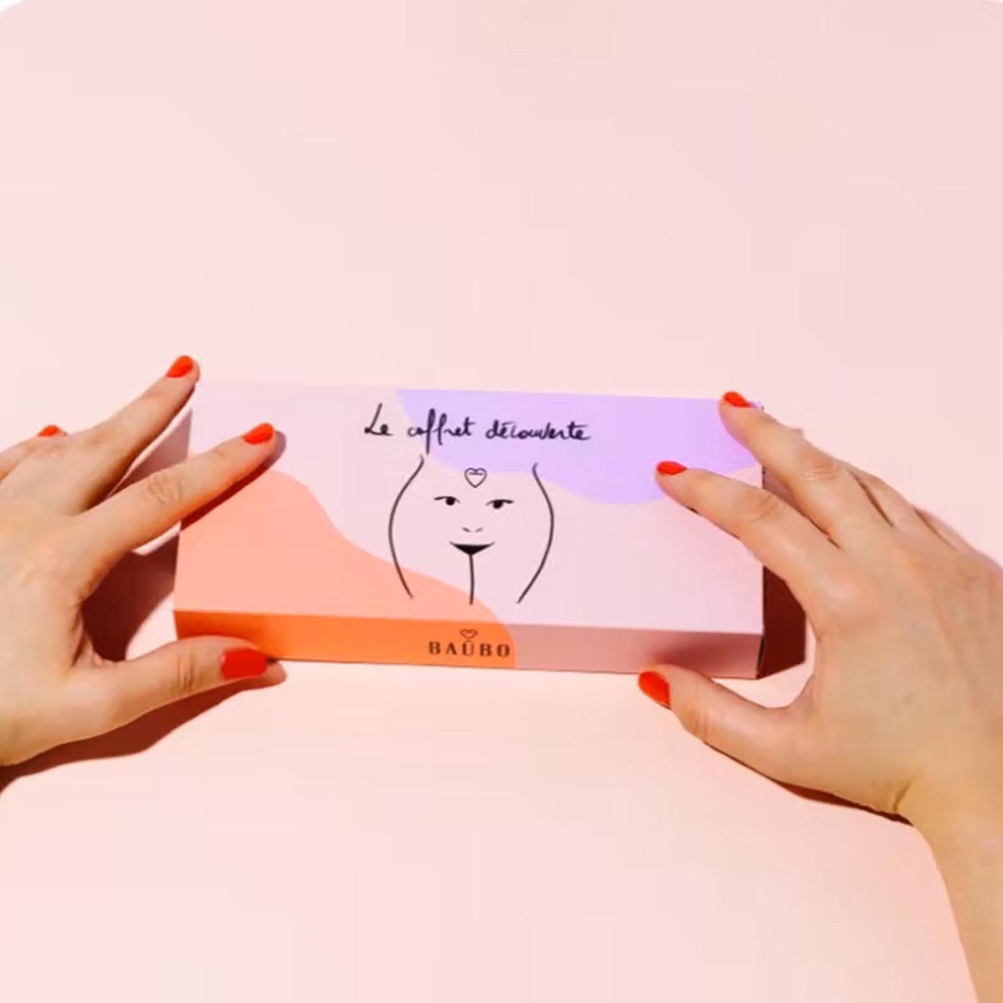 Hände mit rot lackierten Fingernägeln halten die Baûbo „The Discovery Box“ – Ein hochwertiges Bio-Geschenkset für die natürliche Körperpflege in einer kunstvoll illustrierten Verpackung.