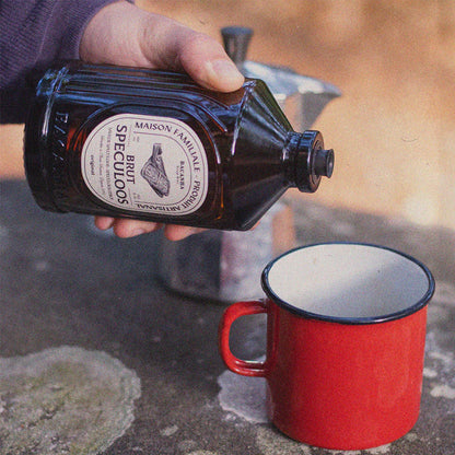 Bacanha Sirop Brut de Speculoos Bio – französischer Bio-Spekulatius-Sirup wird aus der Flasche in eine rote Emaille-Tasse gegossen