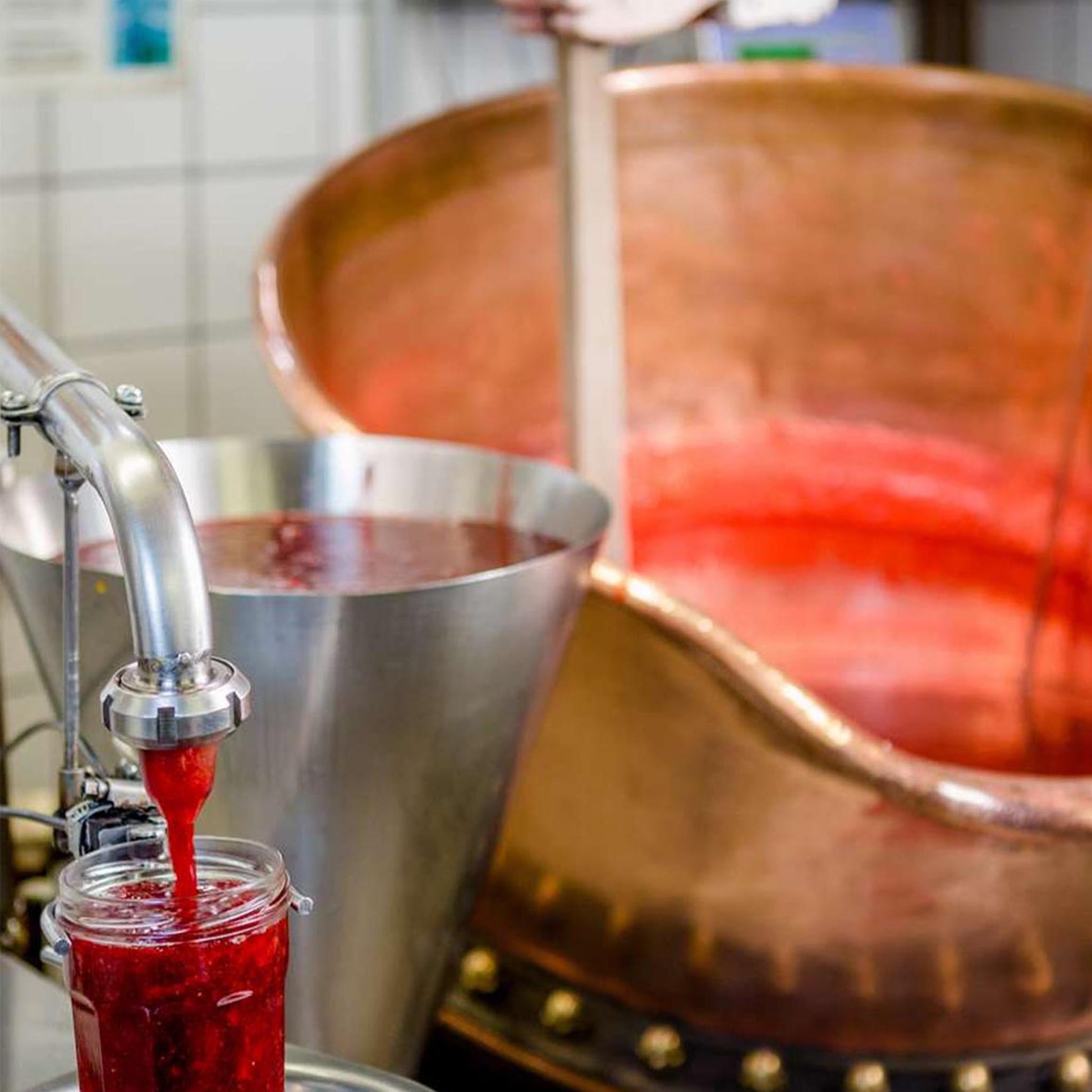 Fruchtige Konfitüre wird aus einem Kupferkessel frisch in ein Glas abgefüllt, traditionelle Manufakturproduktion mit sichtbarer Fruchtstruktur.