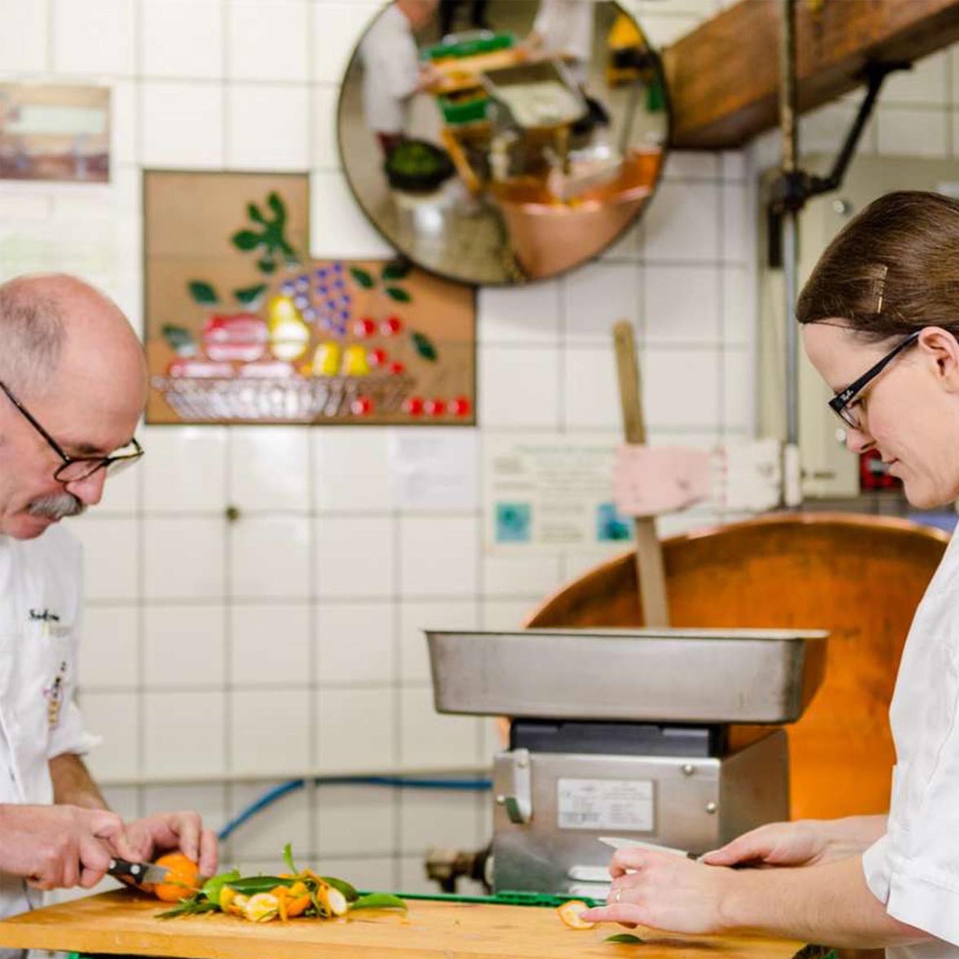 Traditionelle Konfitürenmanufaktur: Zwei Mitarbeiter bereiten frische Früchte von Hand vor, sorgfältiges Schneiden der Zutaten vor einem Kupferkessel für handwerklich hergestellte Konfitüre.