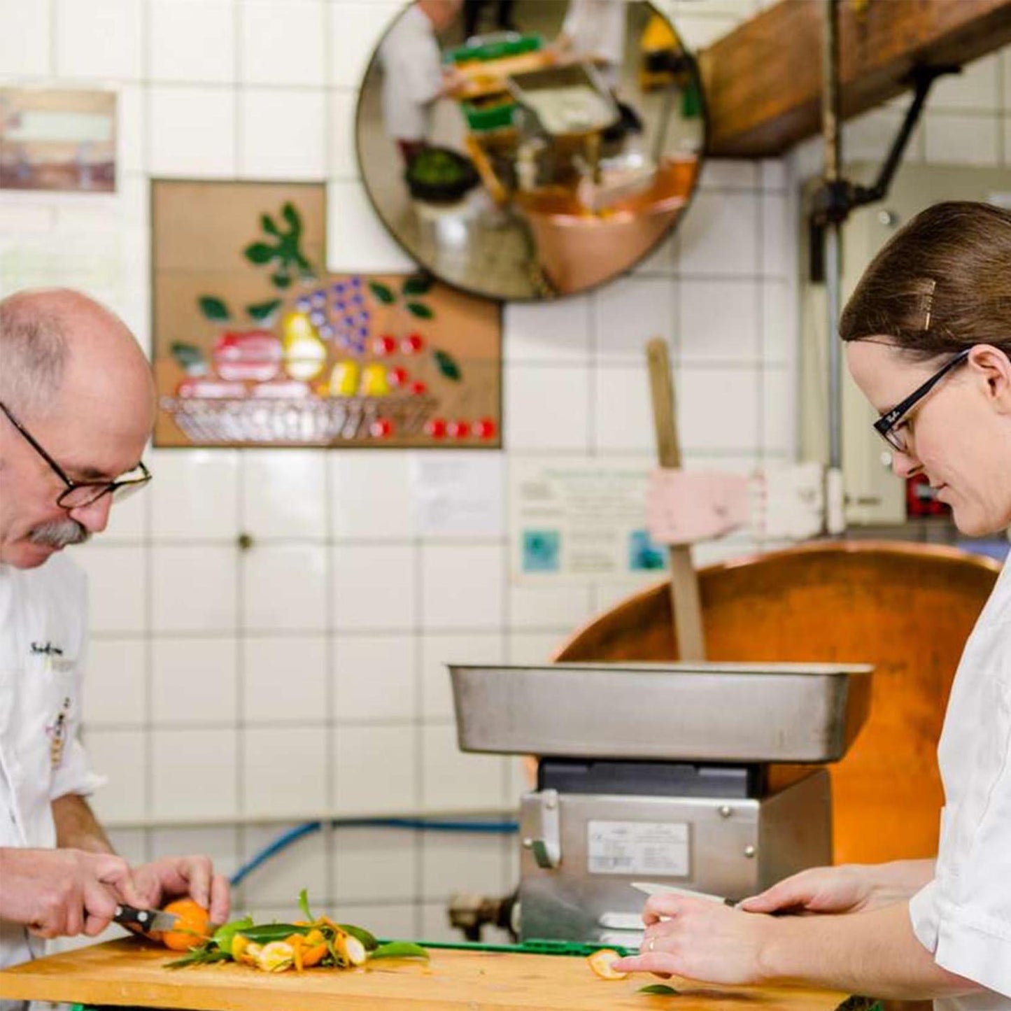 Traditionelle Konfitürenmanufaktur: Zwei Mitarbeiter bereiten frische Früchte von Hand vor, sorgfältiges Schneiden der Zutaten vor einem Kupferkessel für handwerklich hergestellte Konfitüre.