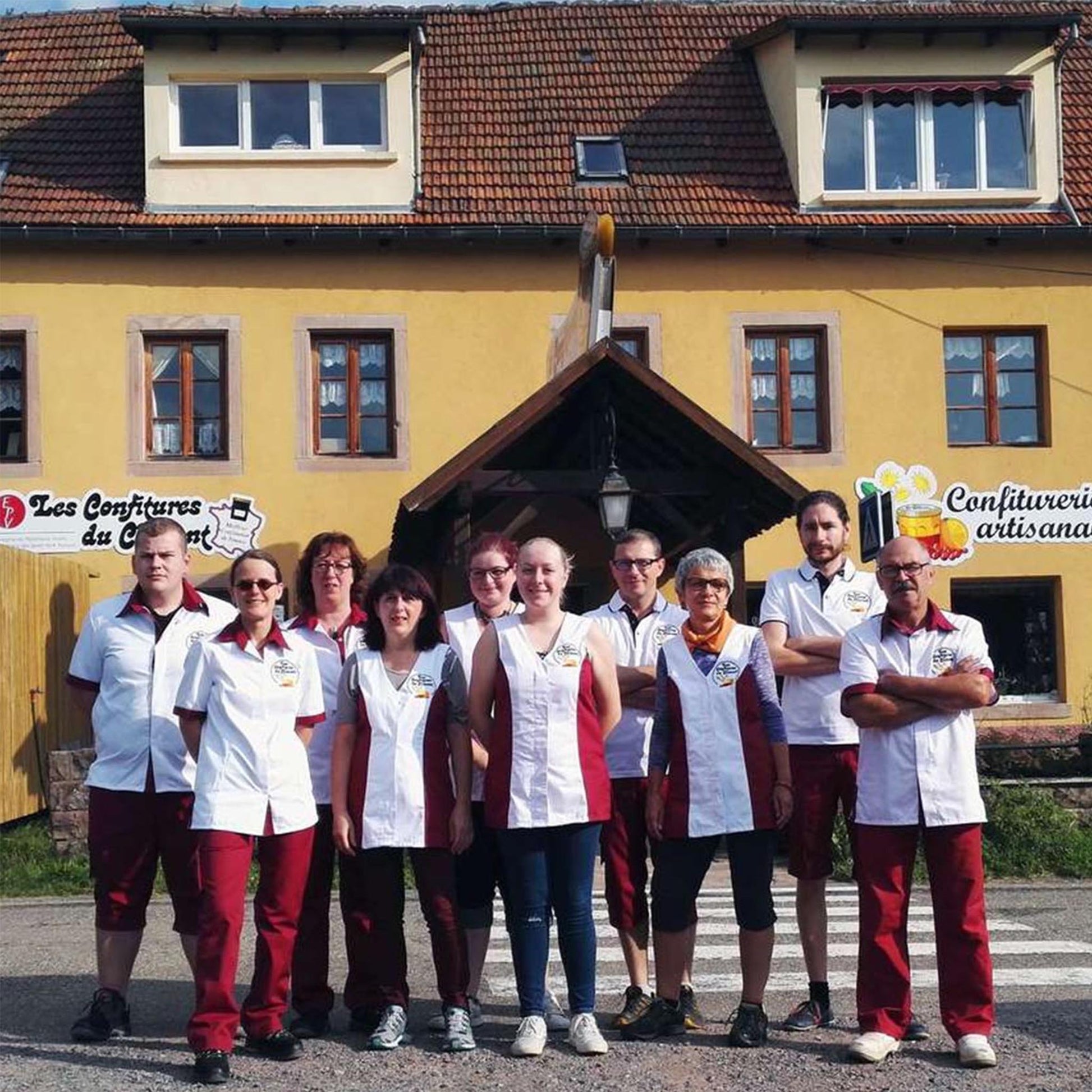 Team der Konfitürenmanufaktur Les Confitures du Climont vor dem Firmengebäude im Elsass, Mitarbeiter in Arbeitskleidung präsentieren handwerkliche Herstellung traditioneller Konfitüren.