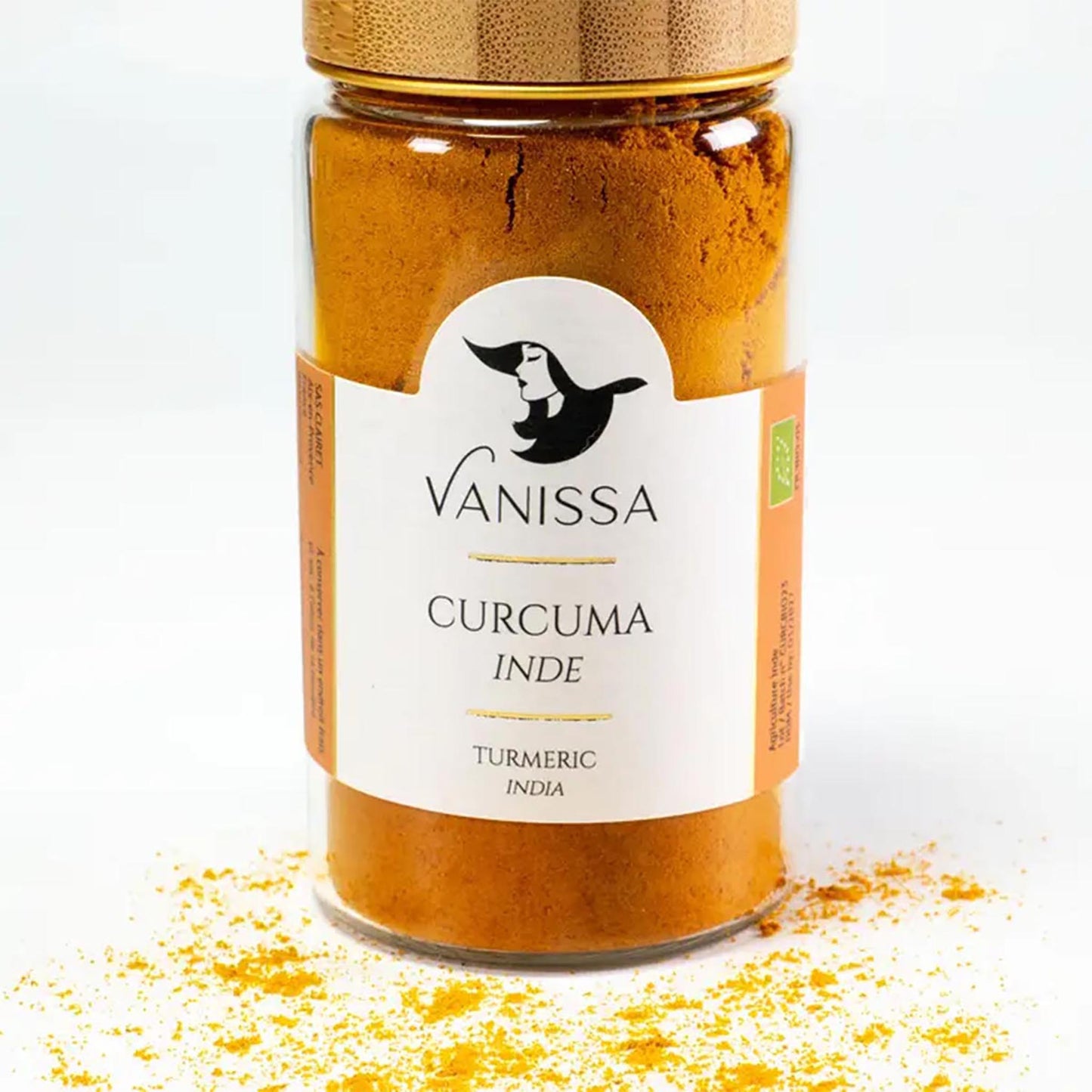 Vanissa Bio-Kurkumapulver aus Indien im 50g Glas mit goldenem Deckel und verstreutem Gewürzpulver auf weißem Untergrund.