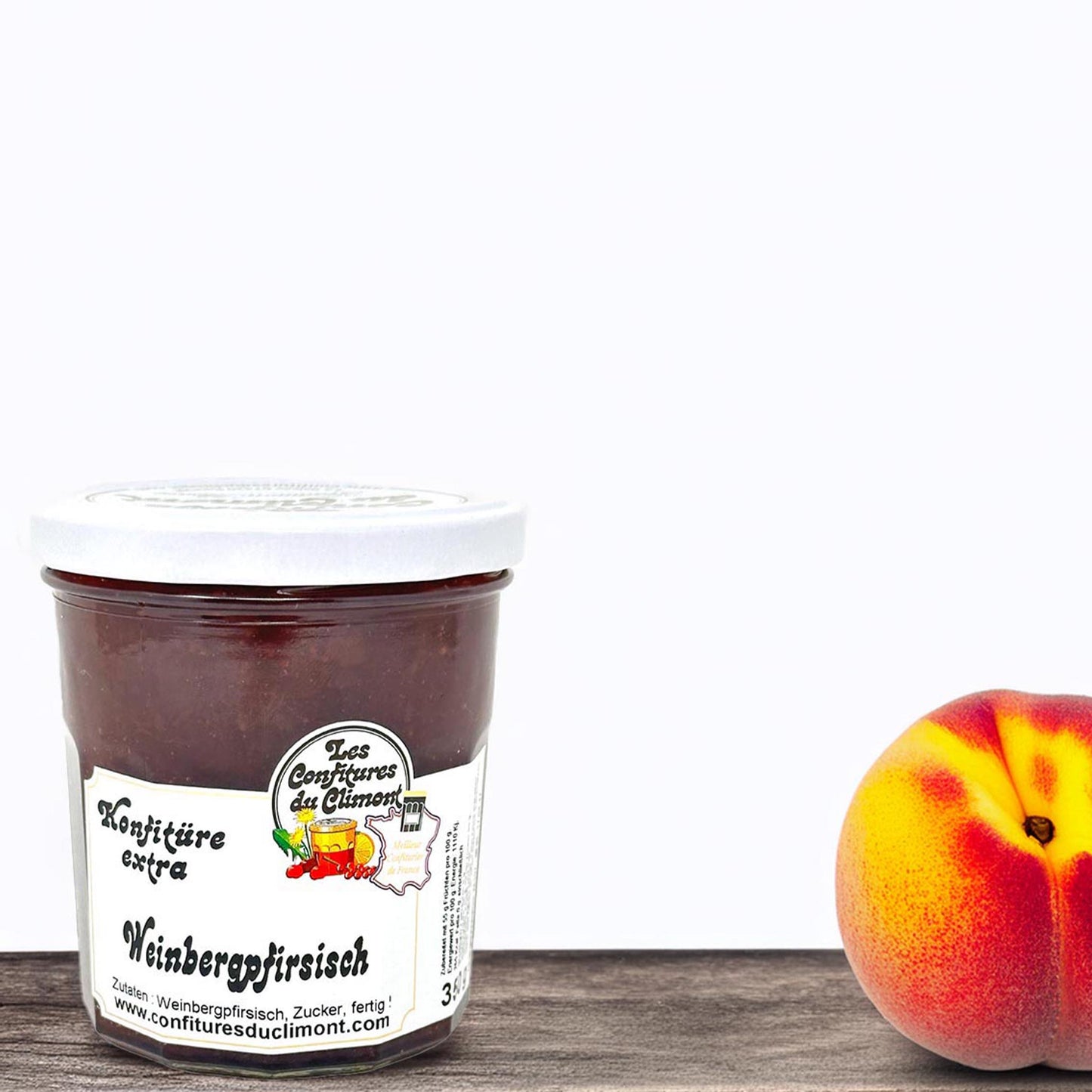 Les Confitures du Climont Weinbergpfirsich Konfitüre extra im Glas auf Holztisch, handwerklich hergestellte französische Konfitüre aus dem Elsass, daneben frischer Weinbergpfirsich, intensiver Fruchtgenuss.