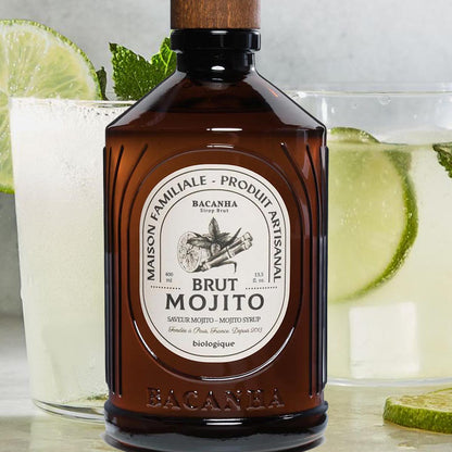 ALT-Text: Bacanha Sirop Brut de Mojito Bio 400 ml in brauner Glasflasche mit Holzverschluss, platziert vor frisch zubereiteten Mojito-Gläsern mit Limettenscheiben und Minze, Bio-Mojito-Sirup für Cocktails und alkoholfreie Getränke