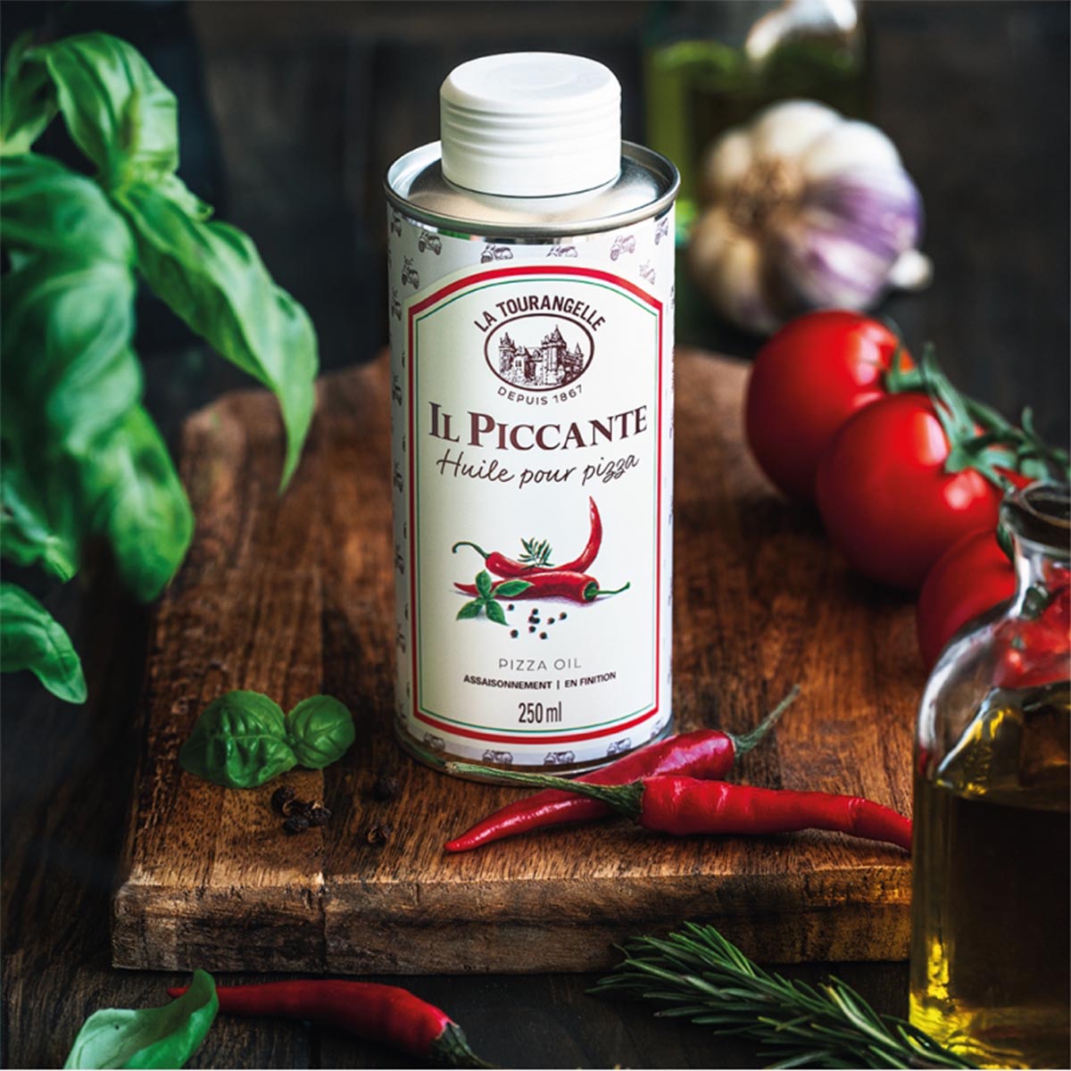 La Tourangelle Il Piccante Pizzaöl – Scharfes Würzöl (250 ml) in der Dose, atmosphärisch arrangiert mit frischen Chilis, Basilikum, Knoblauch und Tomaten